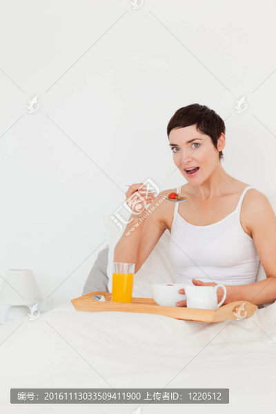 一個(gè)可愛的女人在看著臥室里的相機(jī)時(shí)吃著麥片粥的肖像