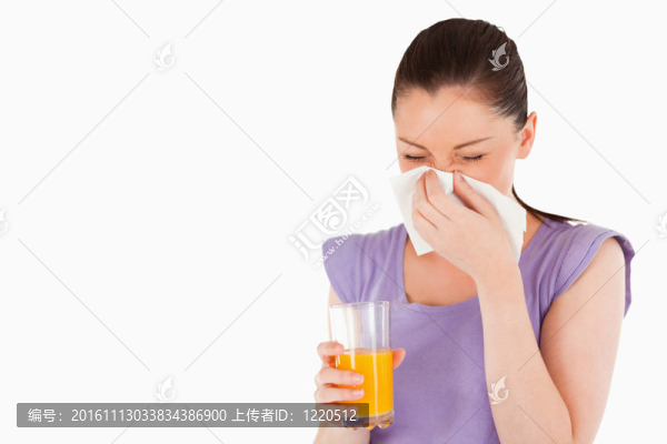 漂亮的女人拿著一杯橙汁和打噴嚏，而站在一個(gè)白色的背景