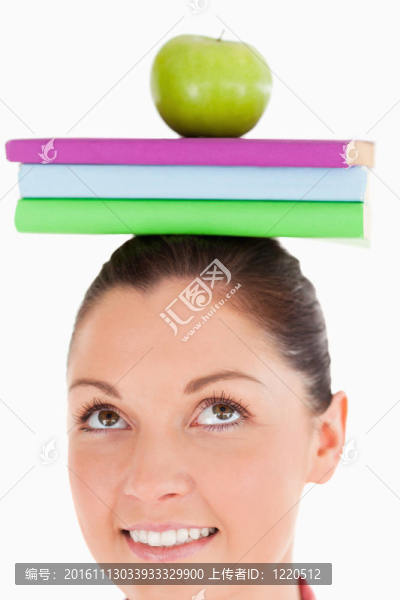 有吸引力的女性拿著蘋果和書在她的頭上，而站在一個白色的背景