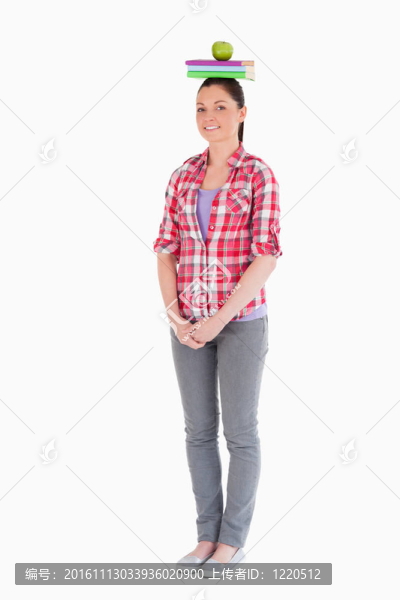 迷人的女性拿著蘋果和書在她的頭上，而站在一個(gè)白色的背景