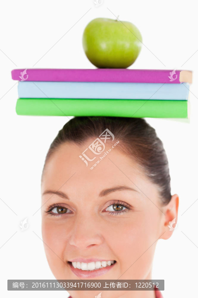 美麗的女性拿著蘋果和書在她的頭上，而站在一個白色的背景