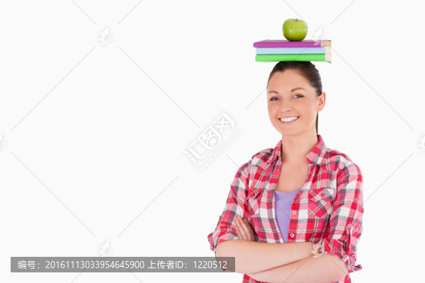 漂亮的女性拿著一個(gè)蘋果和書在她的頭上，而站在一個(gè)白色的背景
