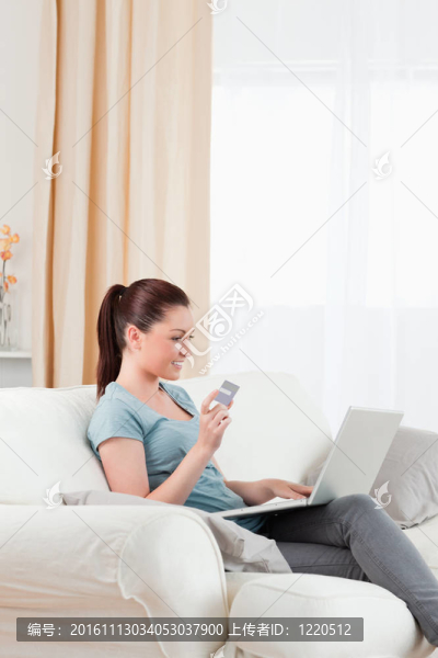 可愛的女人用她的信用卡在線支付，而坐在客廳的沙發(fā)上