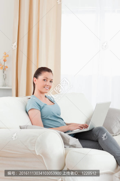 可愛的女人放松與她的筆記本電腦，而坐在沙發(fā)上