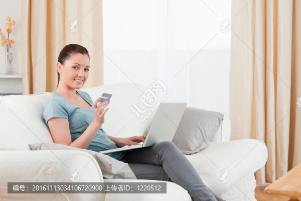 美麗的女人用她的信用卡在線支付，而坐在客廳的沙發(fā)上