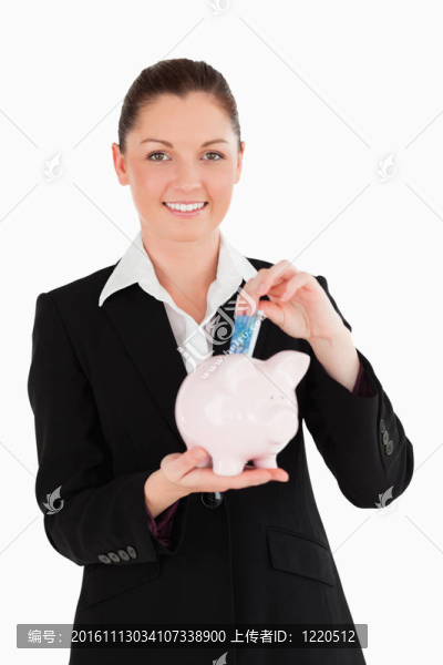 迷人的女人在一個粉紅色的存錢罐里插著鈔票，站在白色的背景上