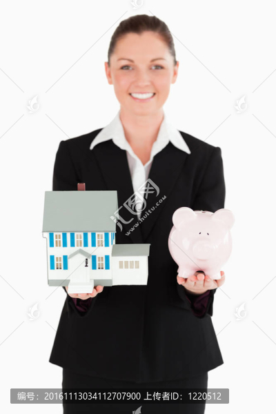 穿著白色的背景，抱著存錢罐和迷你房子的迷人女人