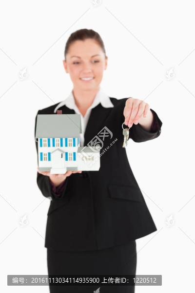 美麗的女人在西裝持有鑰匙和一個微型房子