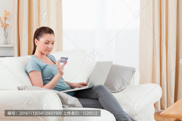 可愛的女人用她的信用卡在線支付，而坐在客廳的沙發(fā)上