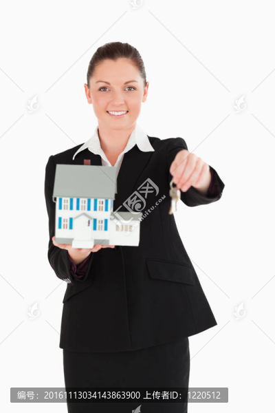 迷人的女人在西裝持有鑰匙和一個微型房子