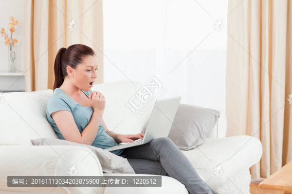 女人坐在客廳的沙發(fā)上，驚訝地用電腦賭博