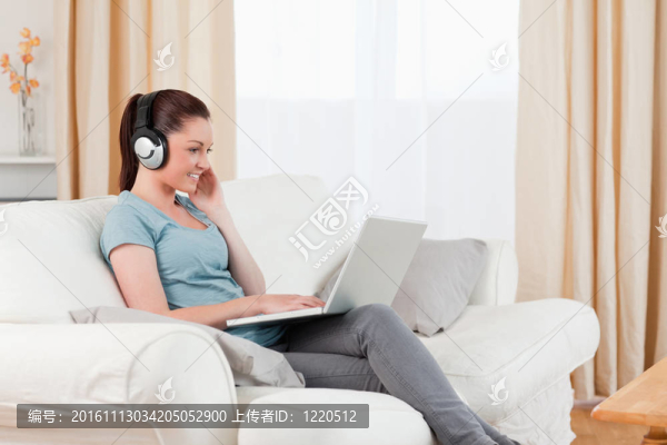 華麗的女人與耳機放松與她的筆記本電腦，而坐在客廳的沙發(fā)上