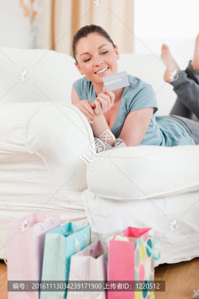 迷人的女人拿著她的信用卡和姿勢(shì)，而躺在客廳的沙發(fā)上