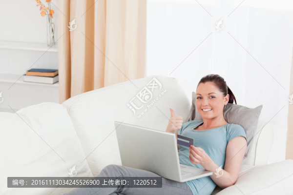 迷人的女性用她的信用卡在線支付，而躺在客廳的沙發(fā)上