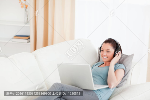 美麗的女性與耳機放松在她的筆記本電腦，而躺在沙發(fā)上的客廳