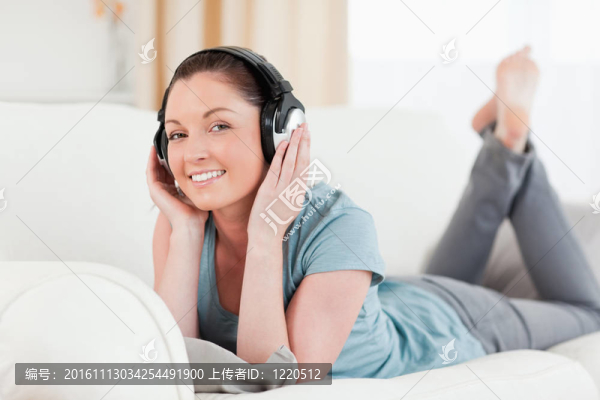 迷人的女人與耳機擺姿勢躺在沙發(fā)上