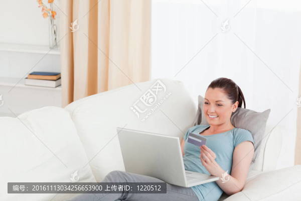 美麗的女性用她的信用卡在線支付，而躺在客廳的沙發(fā)上