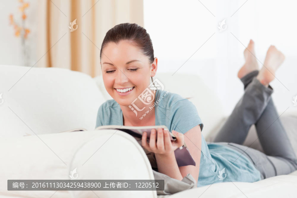 可愛的女人躺在沙發(fā)上看雜志