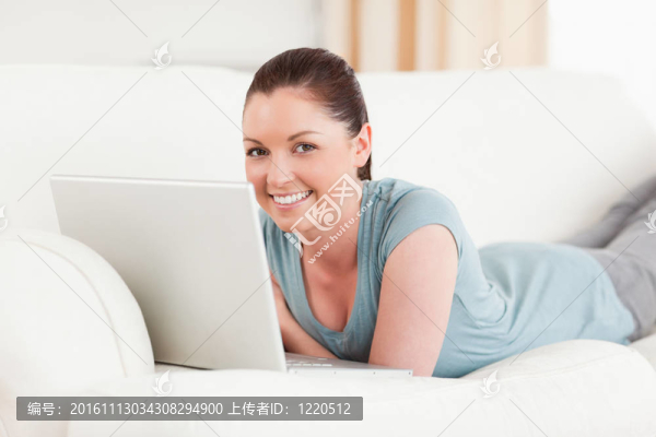 漂亮的女人在客廳躺在沙發(fā)上放松自己的筆記本電腦