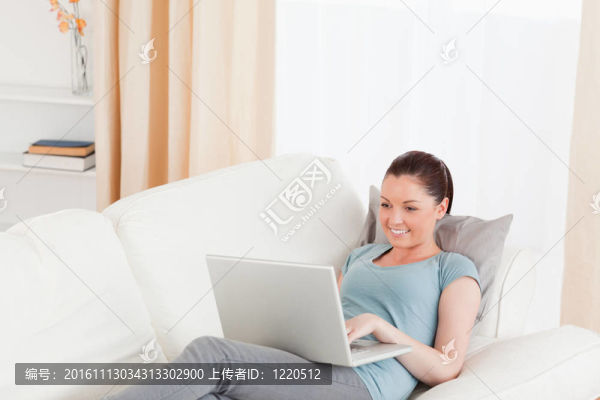 可愛(ài)的女人放松與她的筆記本電腦，而躺在沙發(fā)上