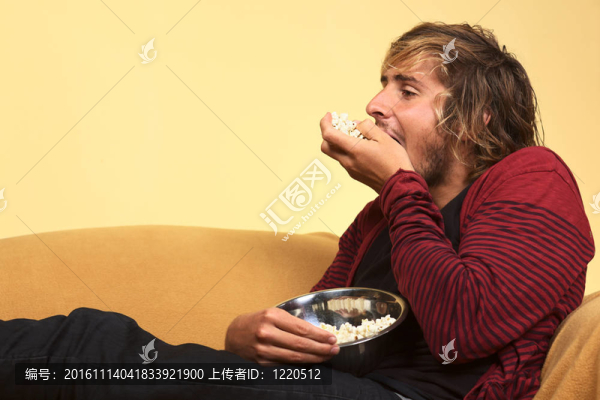 年輕英俊的白人男子吃爆米花（選擇性聚焦；專注于手指；手中的爆米花；和左邊的臉）