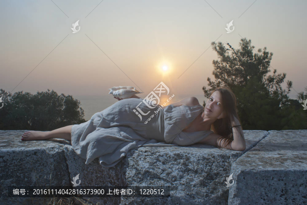 美麗的女孩在日出時抱著漂亮的貝殼
