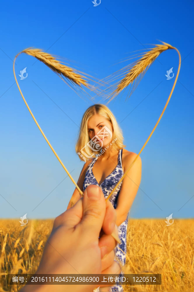 美麗的姑娘站在麥田和心形的邊界
