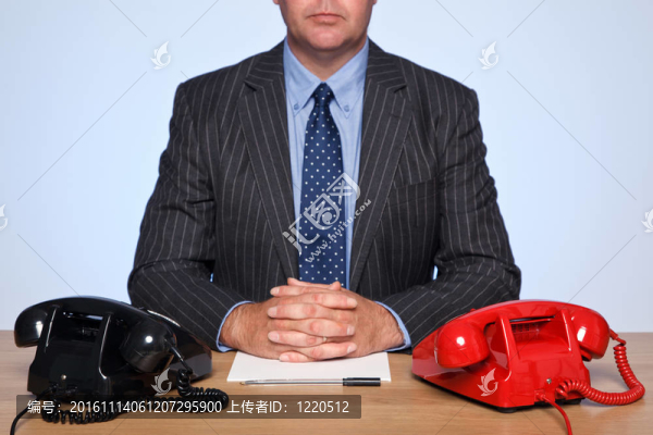 商人坐在桌旁，手里拿著兩個電話。