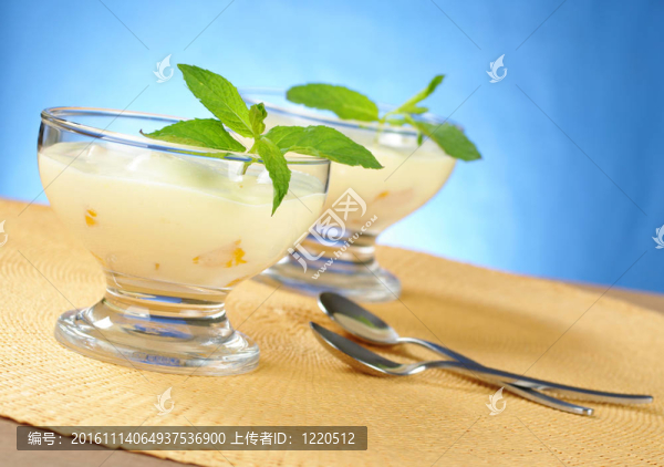 芒果奶油奶酪甜點(diǎn)在玻璃碗與甜點(diǎn)匙在黃色表墊藍(lán)色背景（選擇性的重點(diǎn)，重點(diǎn)放在前面的玻璃和葉子）
