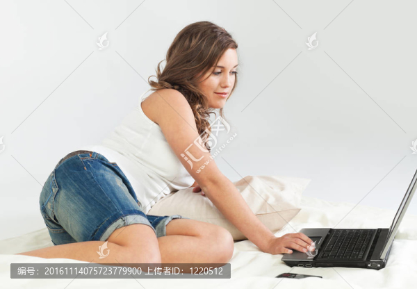 輕松的年輕女子在床上與筆記本電腦