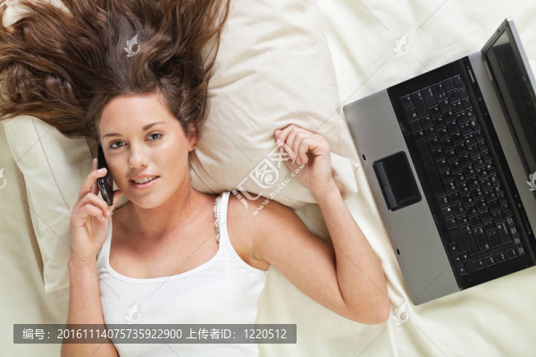 年輕女子在床上用手機和筆記本電腦