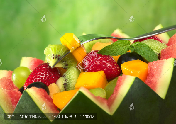 水果沙拉（草莓；獼猴桃；芒果；葡萄）與獼猴桃和芒果叉和薄荷葉在綠色的背景前飾瓜碗（選擇性聚焦；對叉水