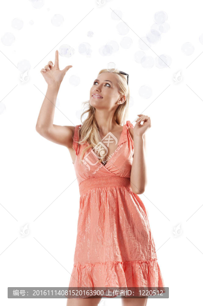 漂亮的年輕金發(fā)女人穿著夏天橙色的衣服站在白色的背景下玩肥皂泡