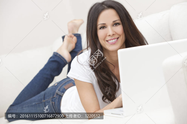 年輕的黑發(fā)女人在家里沙發(fā)上使用筆記本電腦