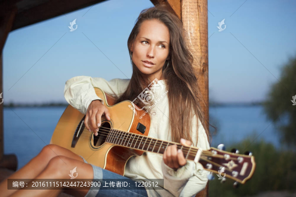 年輕的女人彈吉他在涼亭上的日落