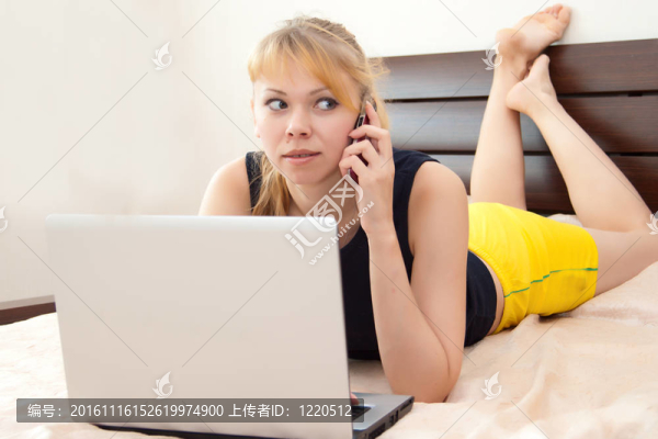 女孩在床上與筆記本電腦和電話(huà)通話(huà)