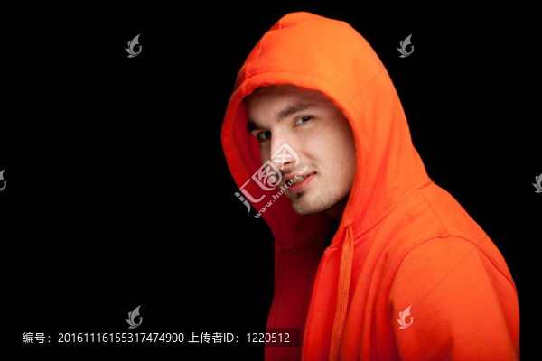 站在年輕人在橙色運動衫和黑色的背景罩；