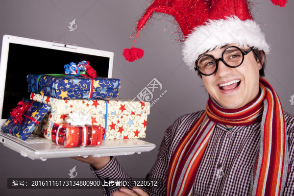 有趣的男子在圣誕帽與禮品盒和筆記本電腦