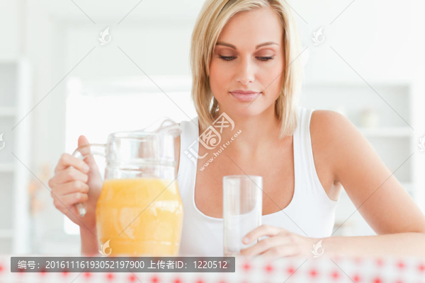 一個(gè)女人坐在廚房桌邊，橙汁和玻璃杯