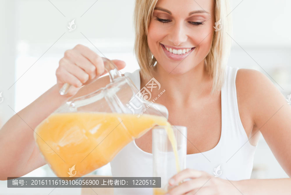 一個面帶微笑的女人坐在廚房里，桌上放著橙汁和玻璃杯.