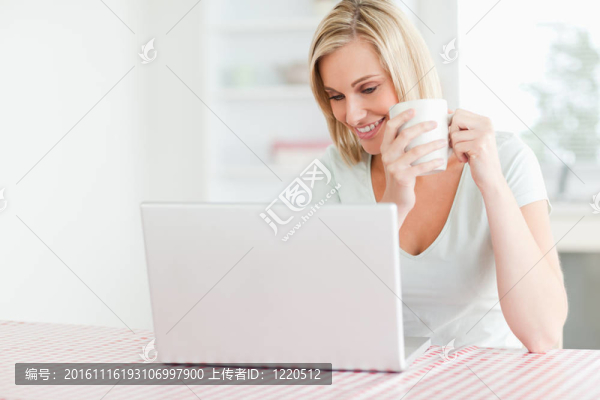 一個拿著咖啡的女人在廚房里看著她面前的筆記本電腦