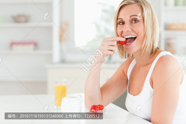 坐在餐桌旁的年輕女人吃草莓-匯圖網(wǎng) www.fosd68.com 坐在餐桌旁的年輕女人吃草莓