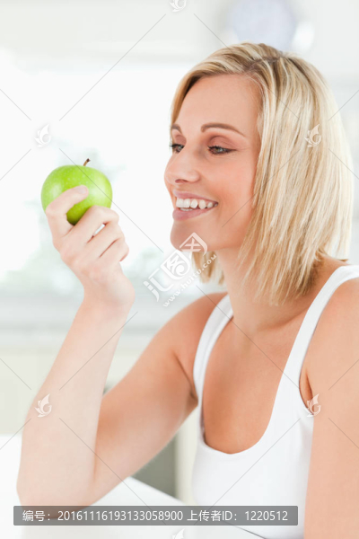 年輕的微笑的女人看著綠色的蘋果