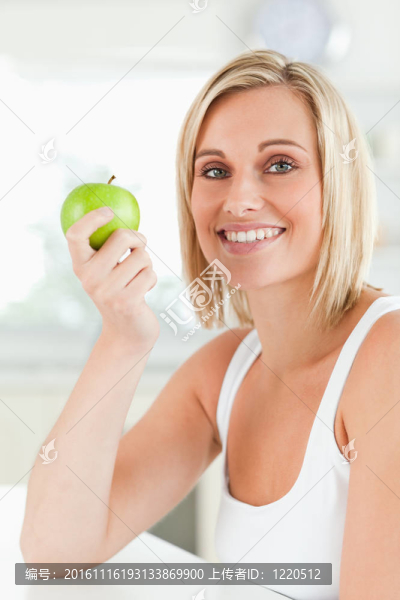 年輕的面帶微笑的女人拿著一個(gè)綠色的蘋果看著相機(jī)