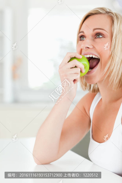 年輕的金發(fā)女人坐在桌子邊吃蘋果