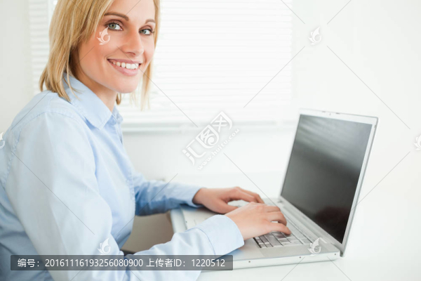 靠近一個美麗的微笑的女商人工作筆記本看著相機在她的辦公室