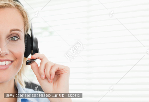 靠近一個(gè)微笑的金發(fā)女商人與耳機(jī)看著相機(jī)在她的辦公室