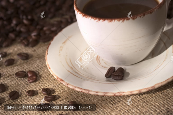 咖啡杯上的咖啡豆，被許多咖啡豆包裹在織物上，稱為黃麻（非常淺的景深；聚焦在茶托上的咖啡豆和一些織物上