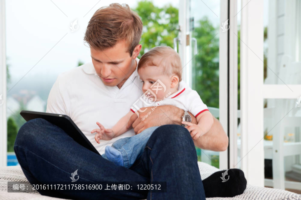 男子使用數(shù)碼平板同時(shí)抱孩子