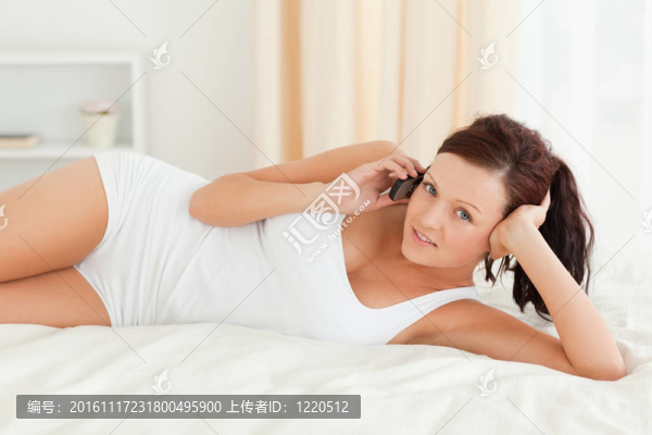 華麗的女人打電話，在她的床上望著鏡頭
